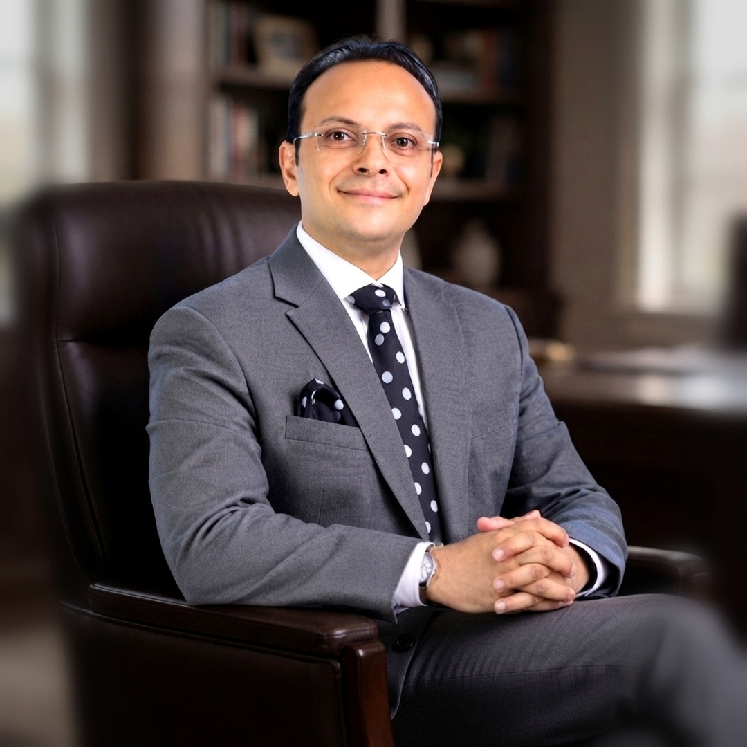 Portrait of a man in a gray suit seated in a chair with a library background